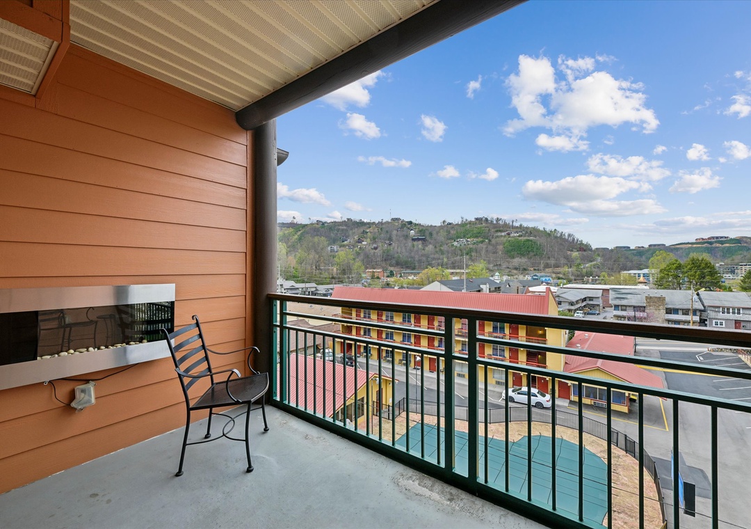 Balcony overlooks colorful buildings and rolling hills under bright blue skies with scattered clouds.