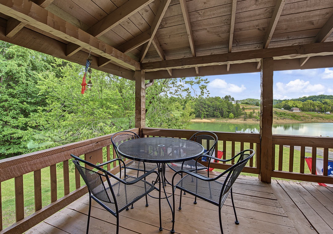 Covered patio with lake and woodland views frames your morning coffee spot. Wooden beams shelter a dining set where you can unwind and take in the peaceful waterfront scenery.