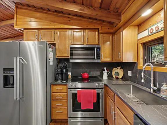 Your vacation kitchen awaits: warm wood cabinets, sleek stainless appliances, and charcoal countertops. Brew coffee, cook your favorite meals, and feel right at home in this inviting, well-equipped space beneath beautiful exposed beams.
