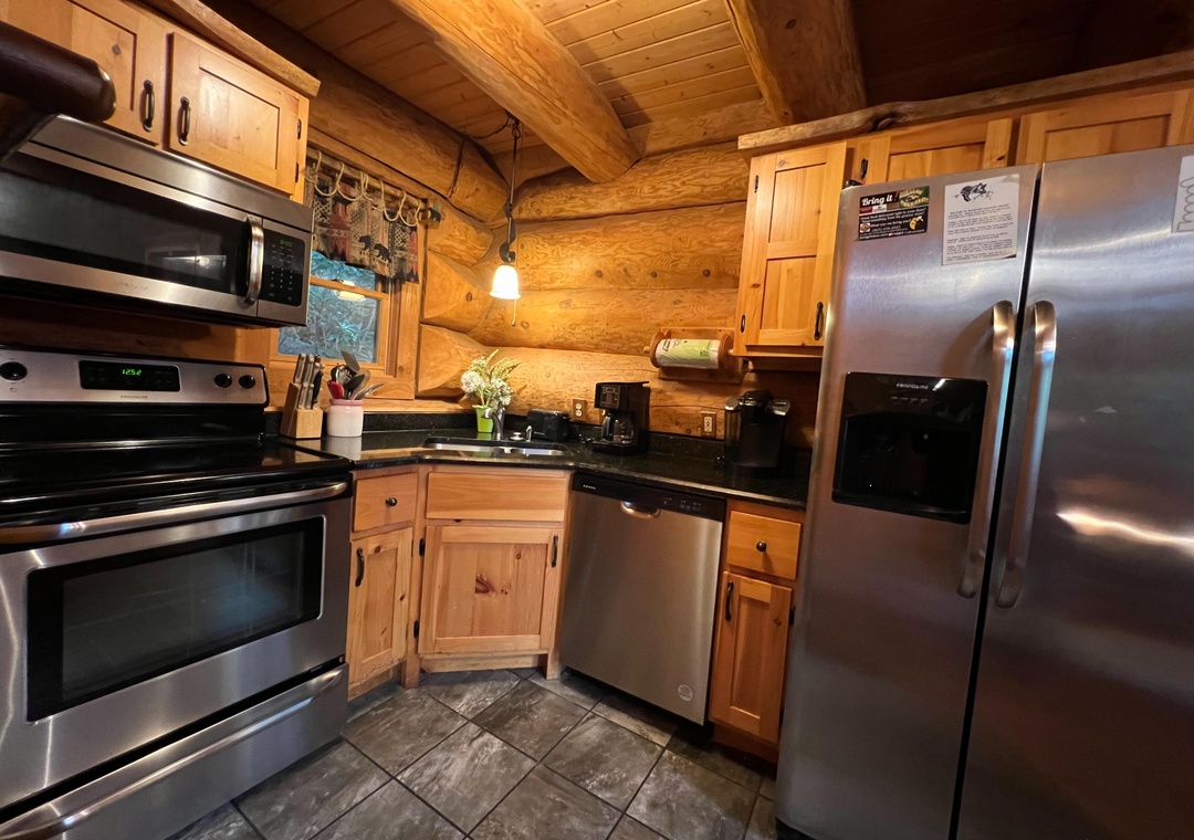 Your rustic-modern kitchen features stainless steel appliances and warm wood cabinetry beneath exposed log beams—perfect for preparing meals in cozy mountain style.
