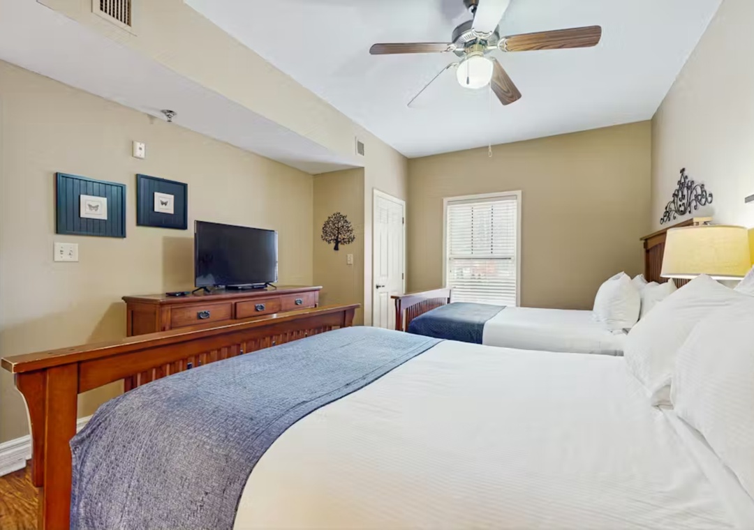 Unwind in your spacious bedroom with two plush beds, warm wood furnishings, and a ceiling fan for your comfort.