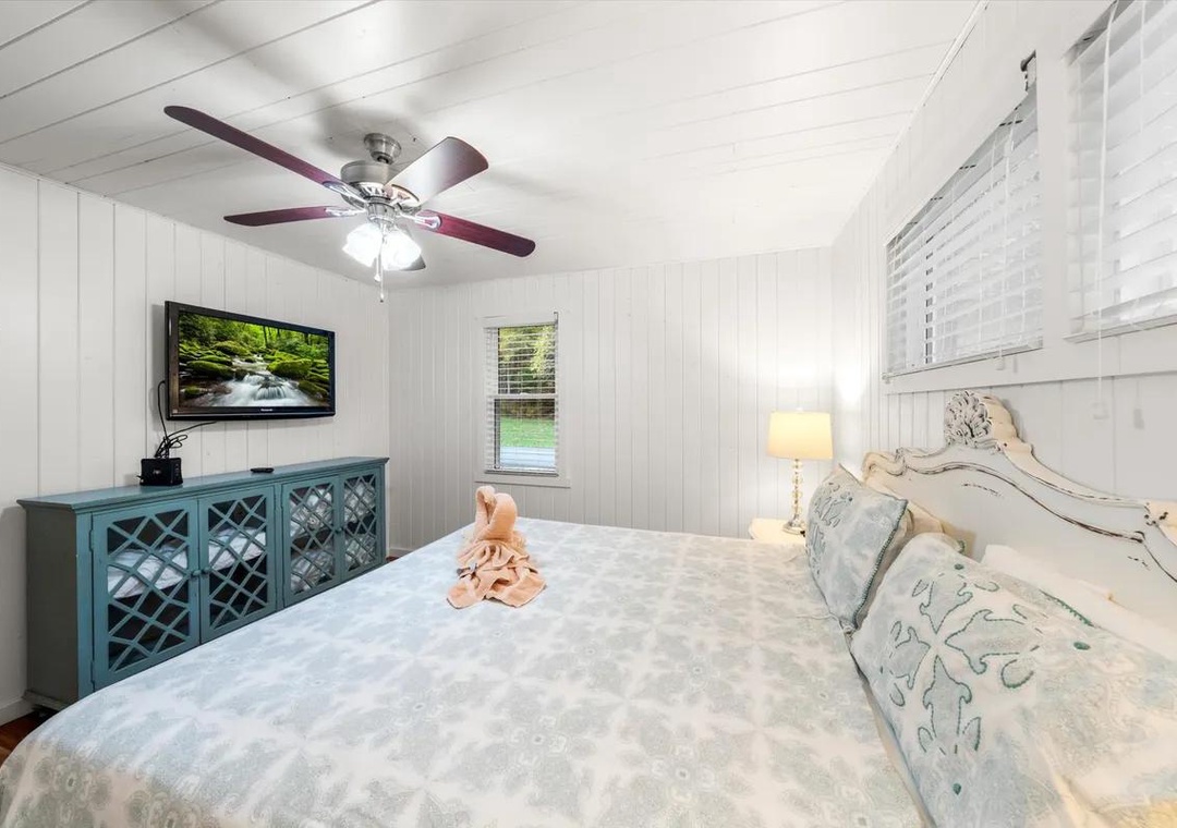 Step into your peaceful retreat with crisp white shiplap walls and a plush bed waiting to cradle you into restful sleep. Soft lamplight and gentle ceiling fan breezes complete the cozy ambiance.