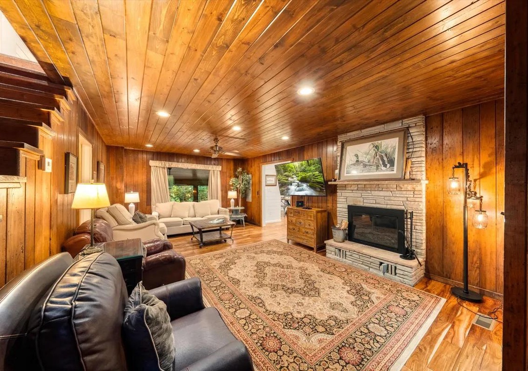 Relax in your spacious, wood-paneled living room where warmth radiates from the classic fireplace and rich knotty pine envelops you. Sink into plush seating under glowing ceiling lights, perfect for evenings in.