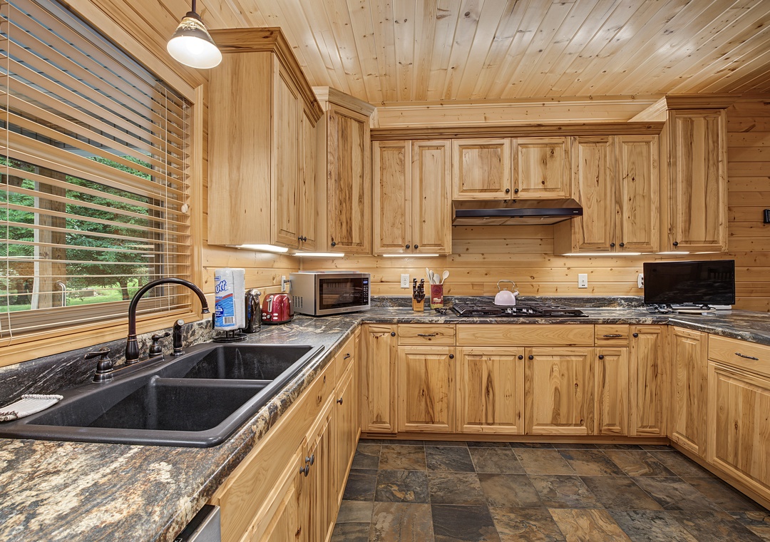 Your fully-equipped kitchen offers warm wood cabinetry, gorgeous granite counters, and modern appliances—perfect for preparing meals while enjoying views of the surrounding greenery through the large window.