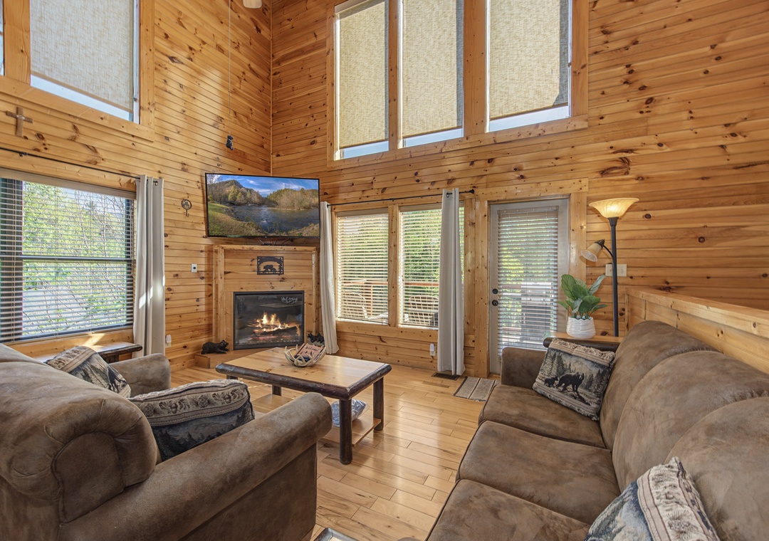 Settle into your cozy cabin living room with warm wood walls,fireplace, and plush seating perfect for mountain getaway relaxation.