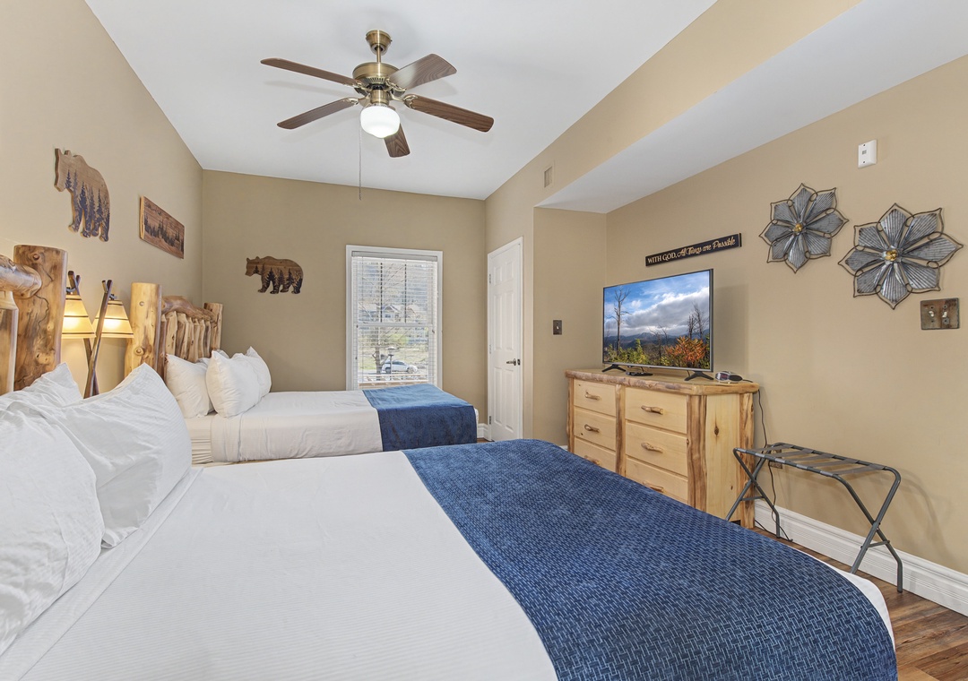 Relax in your cozy mountain-themed bedroom featuring two plush queen beds, rustic wood furnishings, and a ceiling fan for comfort.