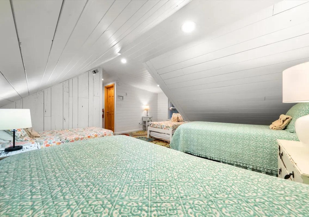 Drift off under bright white shiplap ceilings in this airy loft bedroom, where three cozy beds await your family or group—ideal for those dreamy late mornings and shared laughter.