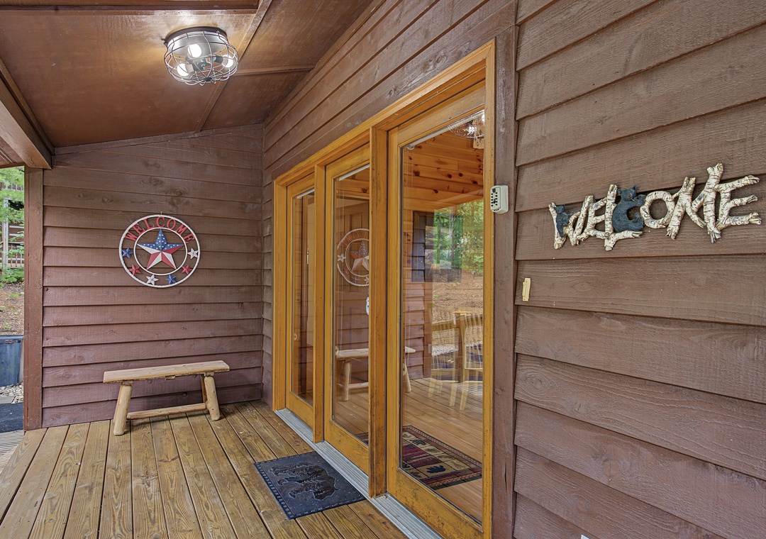 A rustic front entrance with warm wooden finishes and welcoming signage, located in a peaceful natural setting surrounded by trees. The covered entryway offers a charming arrival experience.