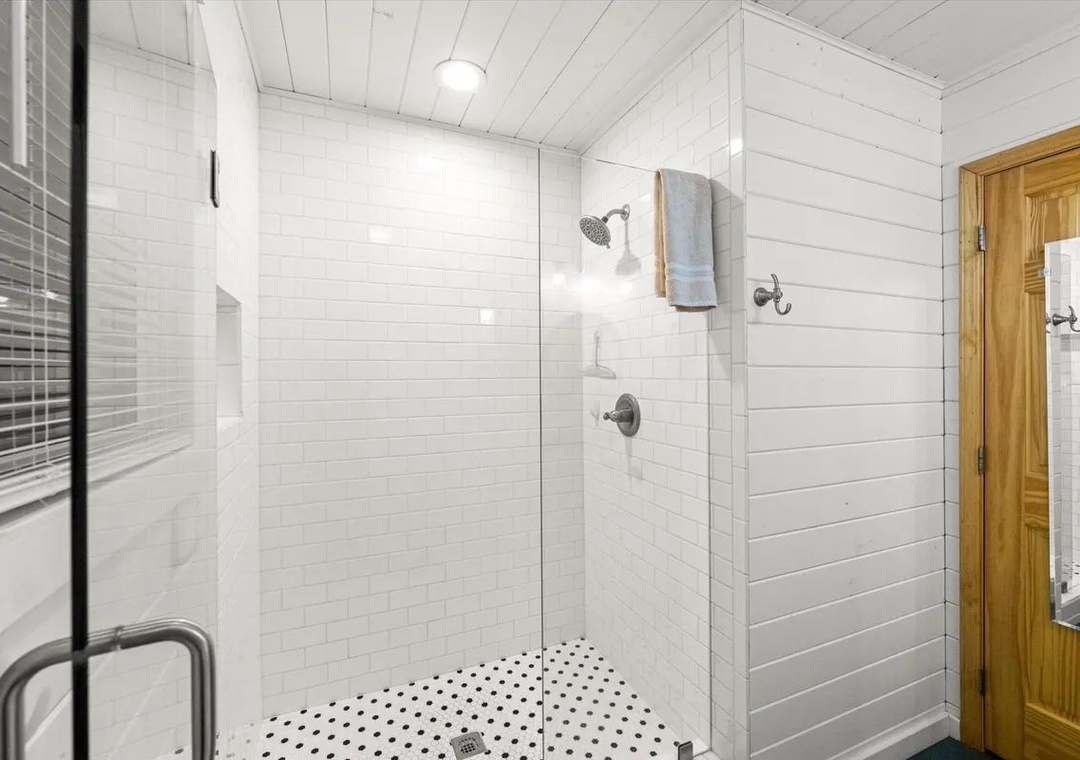 Step into a bright, spotless walk-in shower with classic subway tile walls and a refreshing rainfall showerhead. Fresh towels await your arrival, and the elegant white shiplap and timeless polka-dot floor add farmhouse charm.