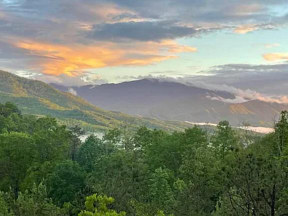 A peaceful mountain landscape showcases rolling hills and lush greenery, with golden clouds painting the evening sky above this serene valley setting.