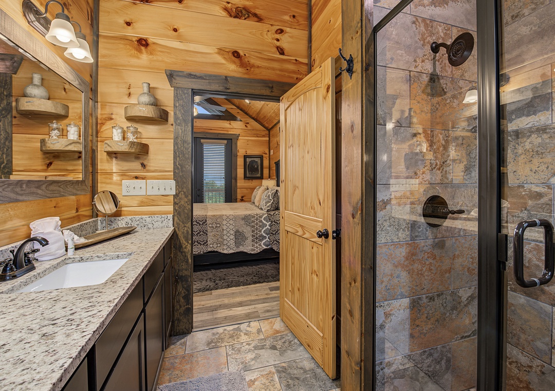 Your private bathroom features a granite vanity, rustic wood accents, and a glass-enclosed shower with natural stone tile—mountain cabin charm meets modern comfort.