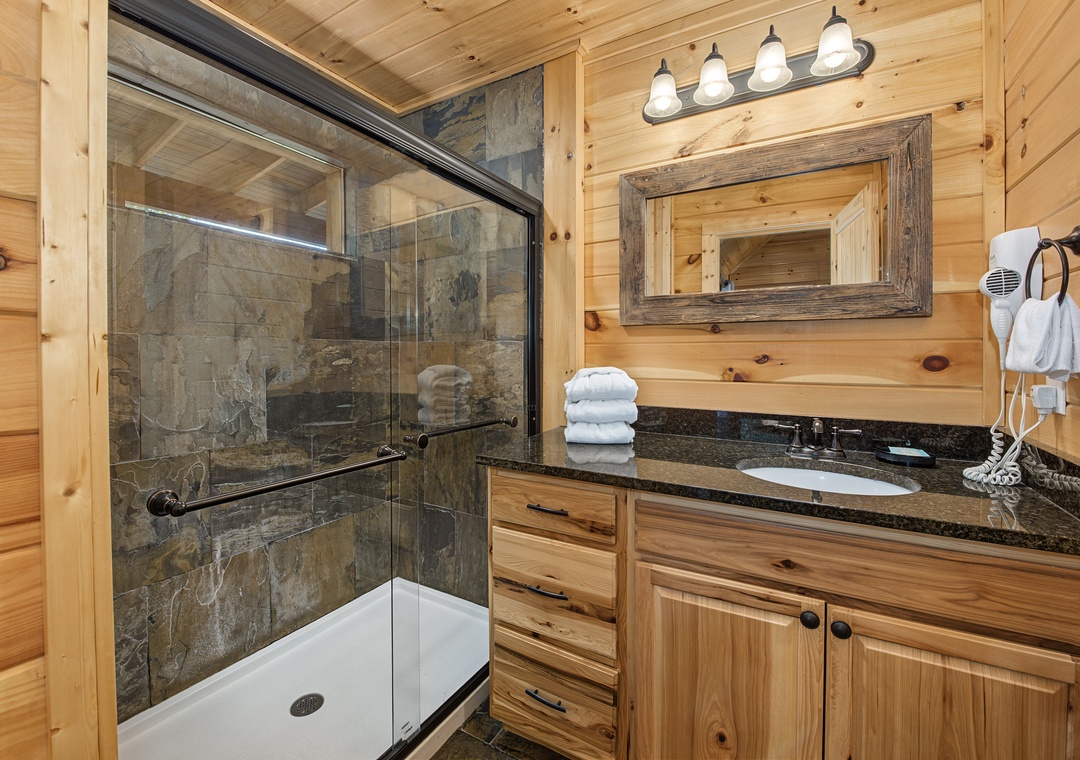 Step into your private bathroom, where rustic wood meets modern comfort. Fresh towels await you on the granite counter, and a spacious stone-tiled shower invites you to unwind after a day of mountain adventures.