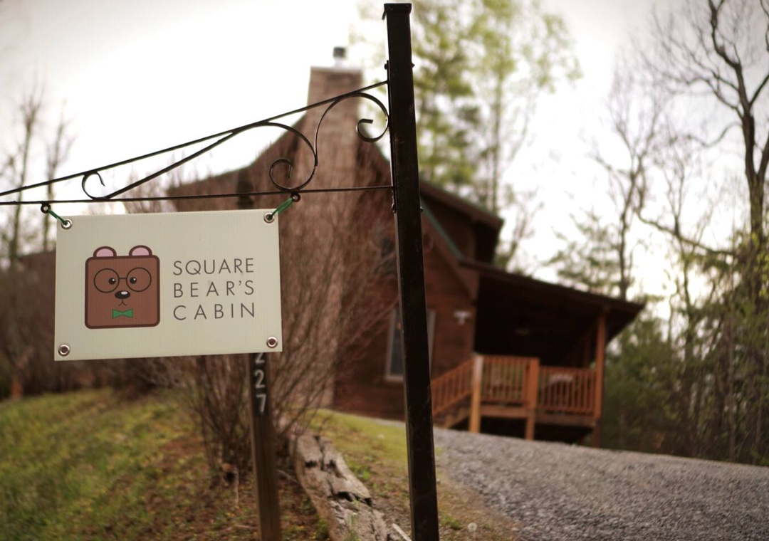 Charming log cabin retreat awaits with welcoming signage marking your arrival at this peaceful wooded sanctuary.