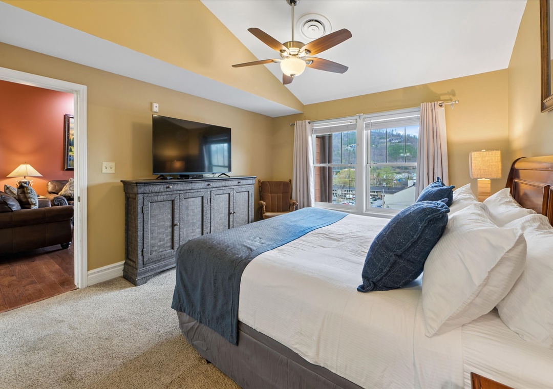 Unwind in your spacious bedroom with plush bedding, gentle ceiling fan, and peaceful views through the large windows.