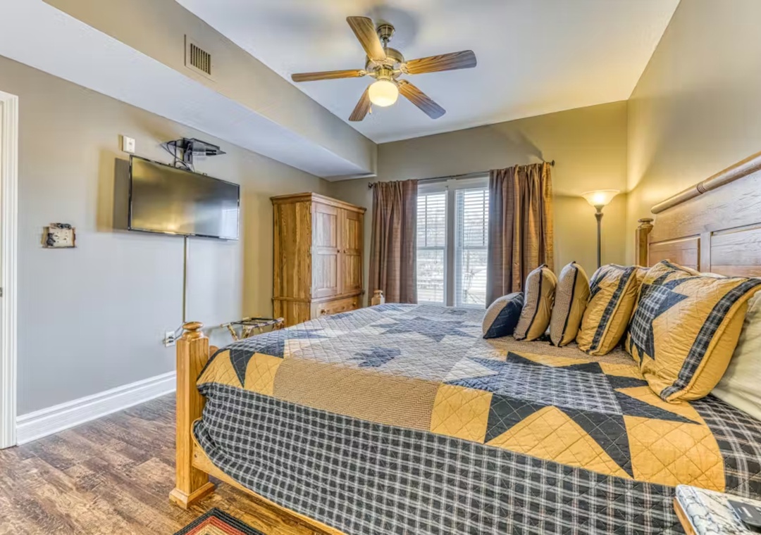 Unwind in your cozy bedroom featuring a plush king bed, warm country quilts, and modern amenities like wall-mounted TV and ceiling fan comfort.