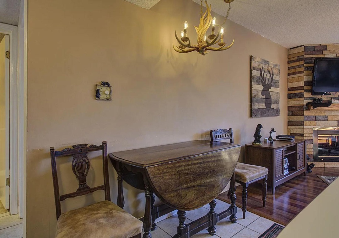 Gather around your rustic dining table beneath the antler chandelier, with cozy fireplace warmth and charming cabin decor creating perfect moments.