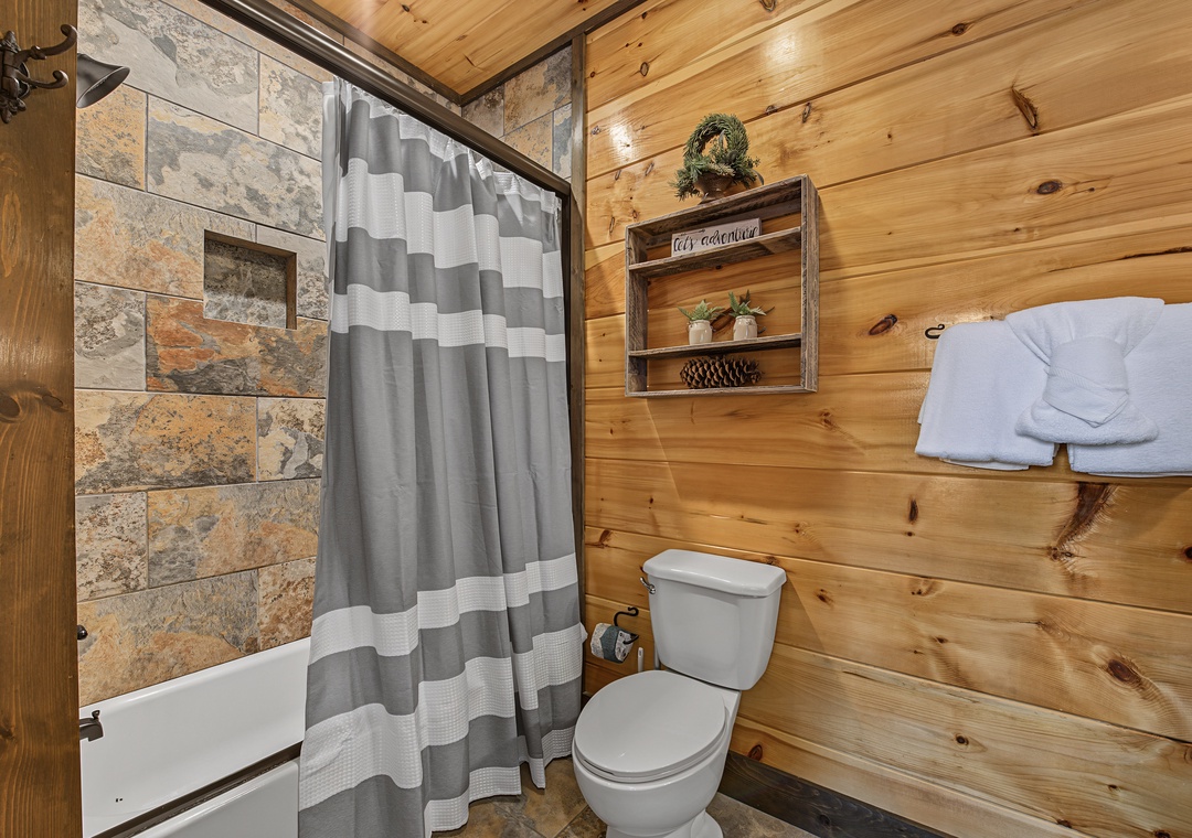 Unwind in this rustic yet modern bathroom featuring warm wood walls, stone tile shower, and plush towels ready for your arrival—cozy comfort after a day of mountain adventures.