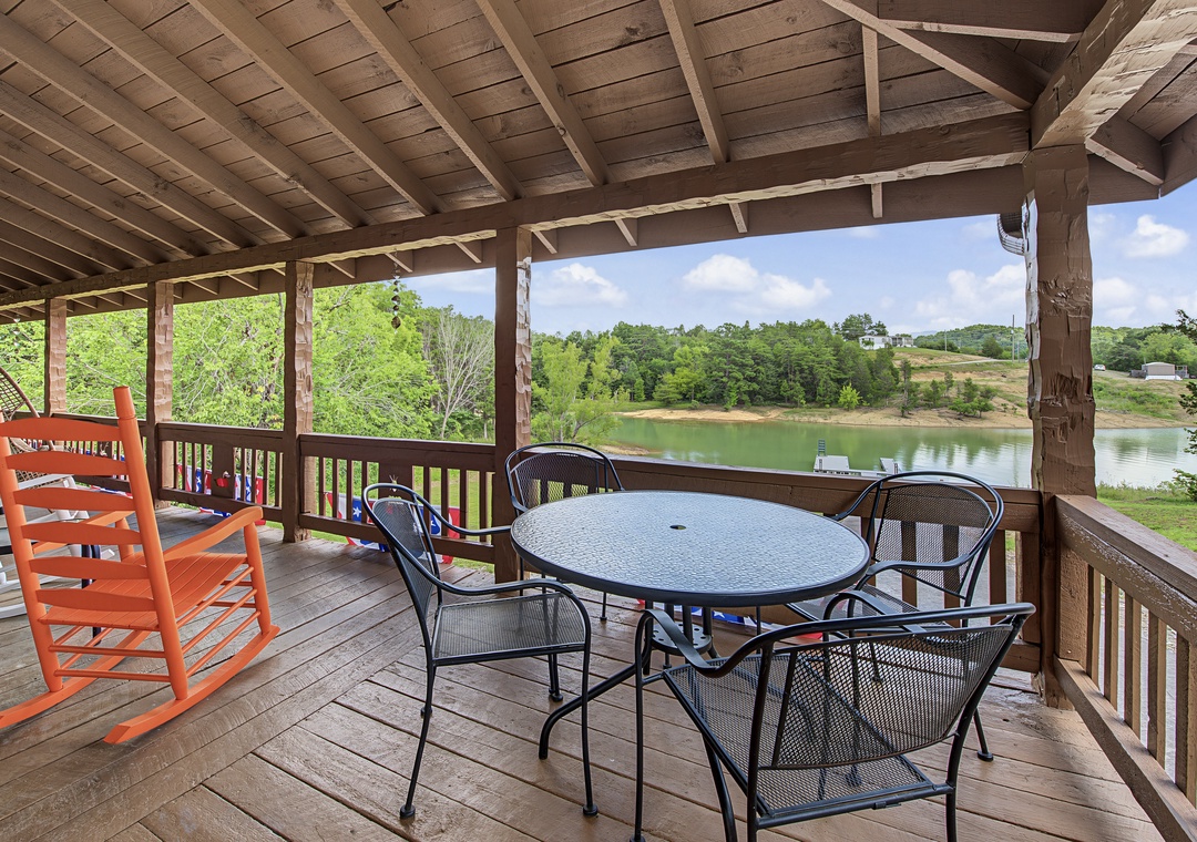 Imagine your morning coffee here—this covered deck overlooks a serene lake and lush greenery. Gather around the dining table or rock gently in the chairs as you soak in the peaceful water views.