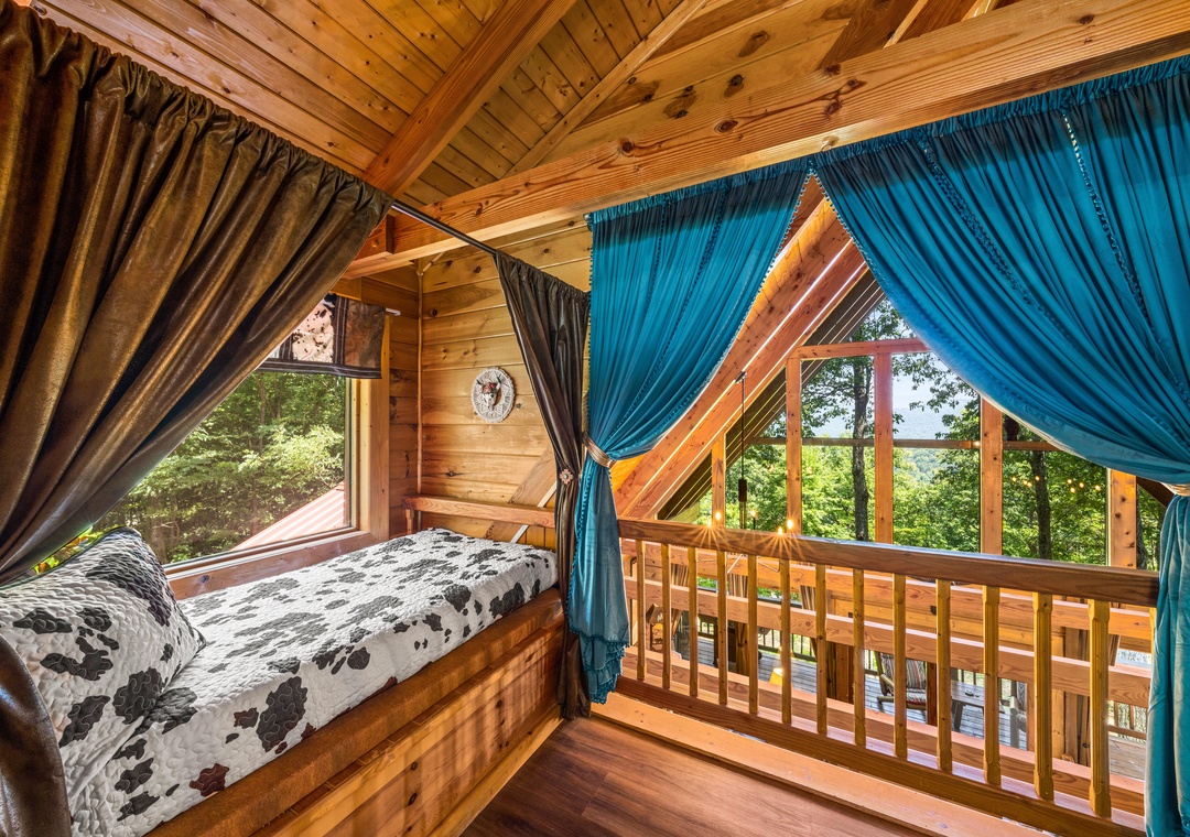 Wake up to forest views from your lofted sleeping nook, where warm wood beams and colorful curtains frame peaceful treetop vistas through the expansive windows.