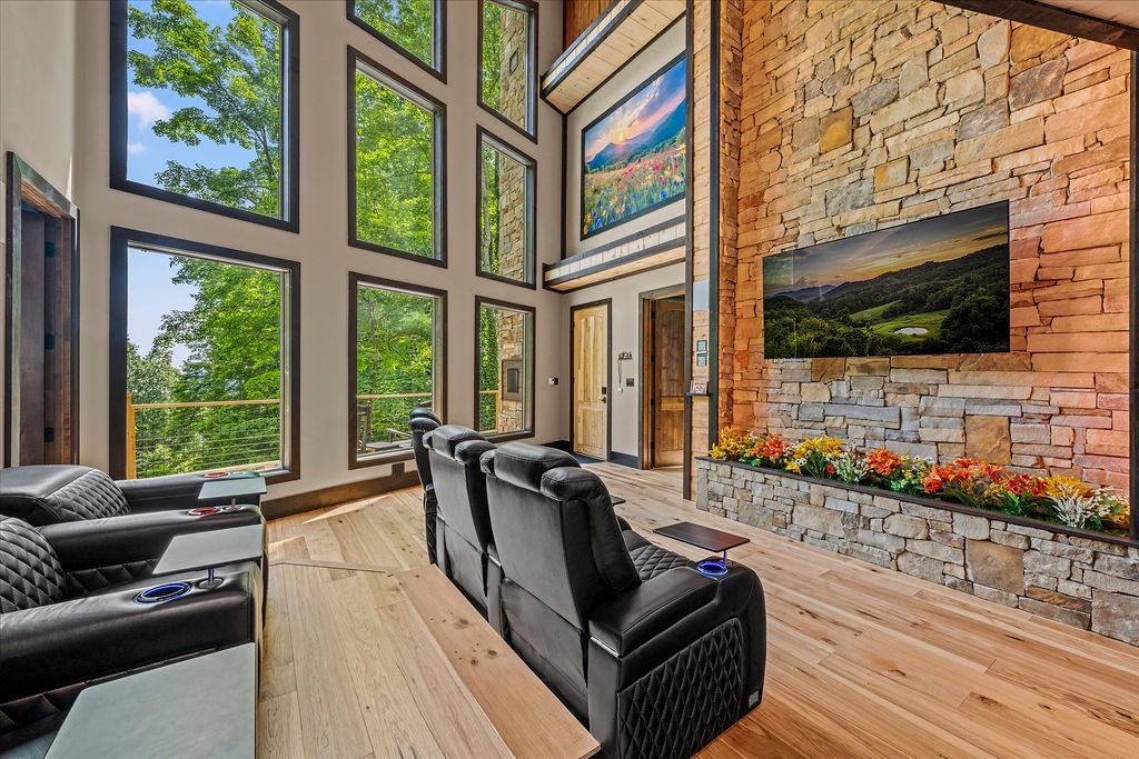 Sink into plush seating as sunlight pours through soaring windows, revealing lush forest views. The stone fireplace anchors the space with rustic warmth.