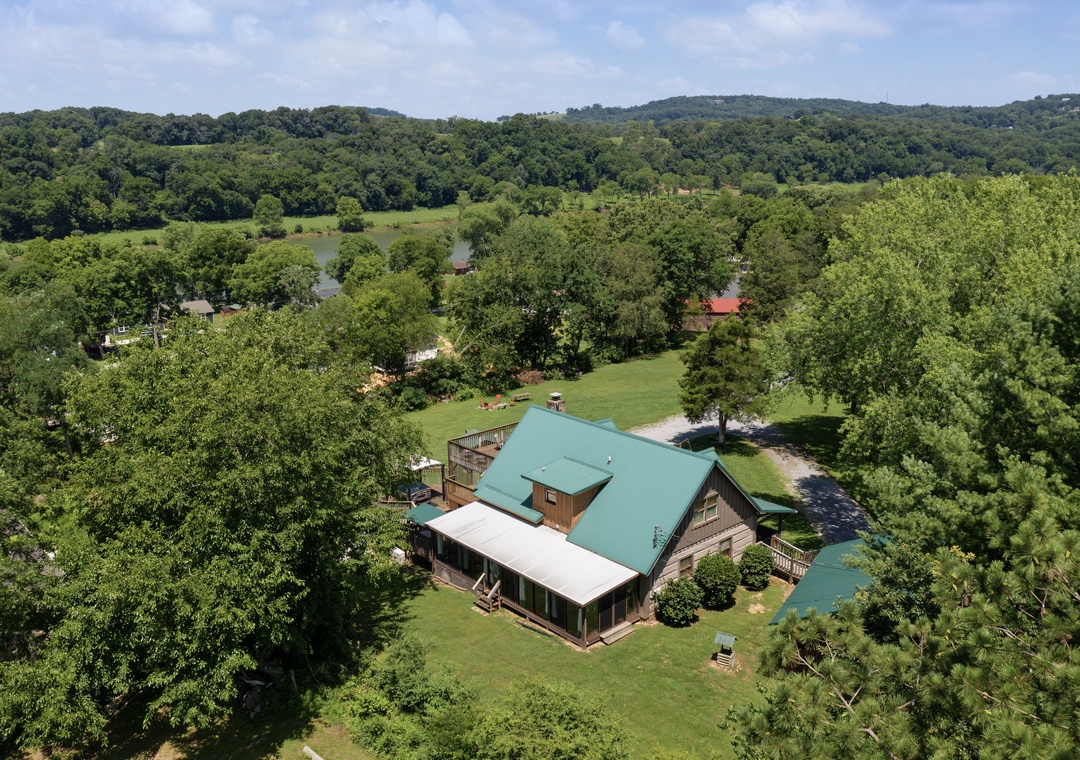 Aerial view of a charming vacation rental nestled among rolling hills and lush greenery, surrounded by peaceful countryside and neighboring properties in a scenic natural setting.