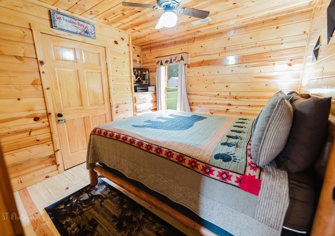 Unwind in your cozy cabin bedroom with warm knotty pine walls, a comfy bed draped in Southwest-inspired linens, and soft natural light streaming through the window—your perfect mountain retreat awaits.
