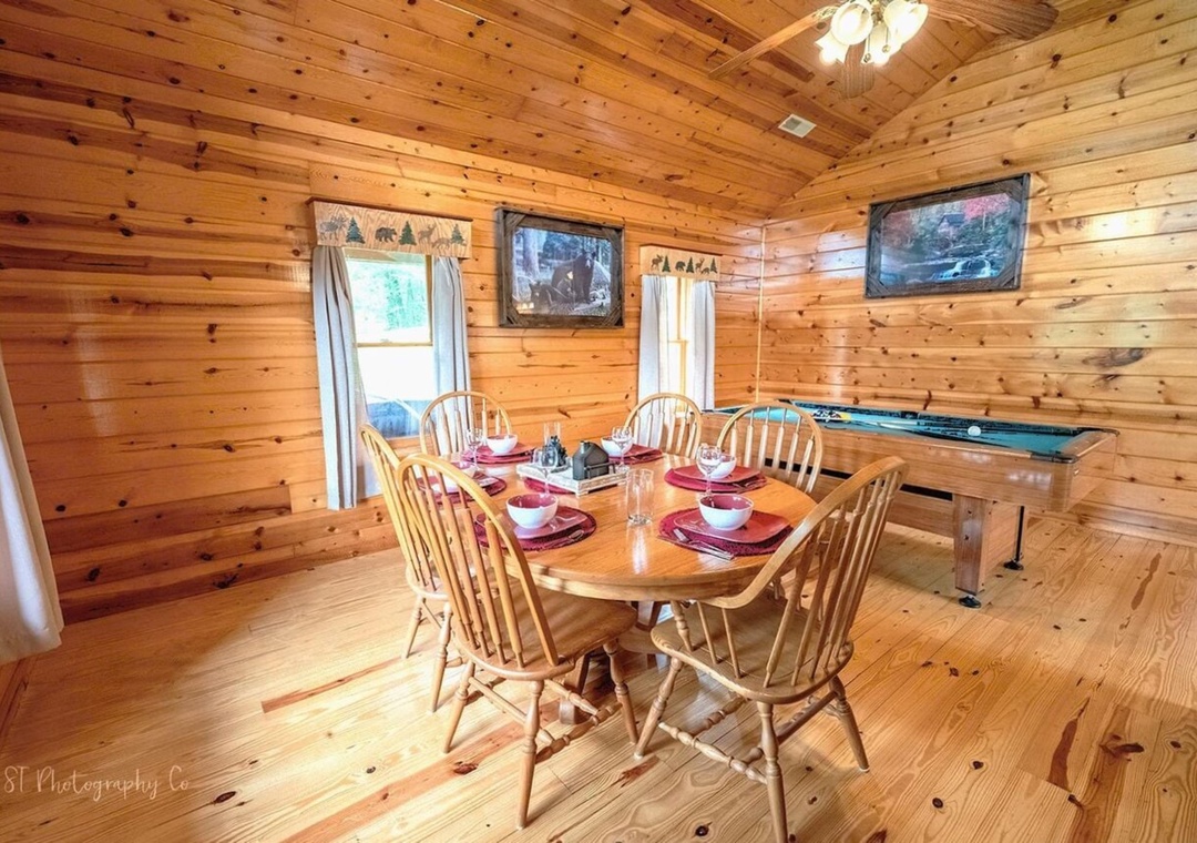 Gather around your rustic wood dining table in this cozy cabin, set for six with charming dishware. Natural light fills the room, and a pool table awaits your fun.