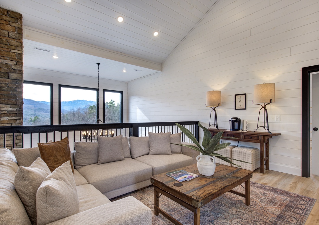 Unwind in your spacious loft living room with mountain views, cozy sectional seating, and rustic stone fireplace for perfect evenings.