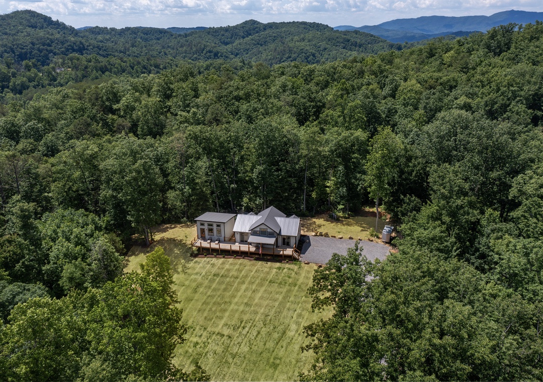 Aerial view of a private mountain retreat surrounded by dense forest and rolling peaks, offering secluded tranquility in a natural landscape.