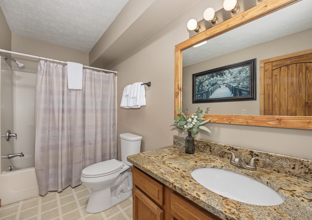 Step into your private bathroom with warm wood accents, granite countertops, and fresh towels waiting for you. The soft lighting and thoughtful touches create a serene space to refresh.