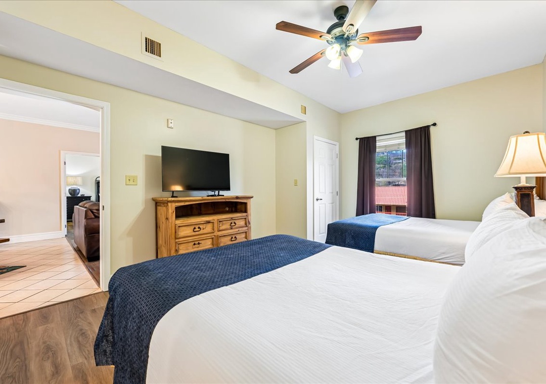 Unwind in your spacious bedroom featuring two comfortable beds, warm wooden furnishings, and a gentle ceiling fan for perfect comfort.
