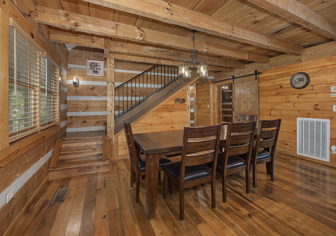 Gather around the solid wood dining table under rustic timber beams, perfect for family meals and game nights in this warm, open-plan cabin retreat.