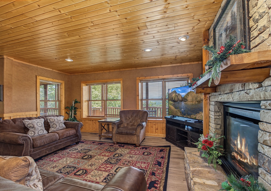 Curl up in your cozy living room with soaring wood ceilings and a warm stone fireplace. Large windows frame the lush surroundings, filling the space with natural light.
