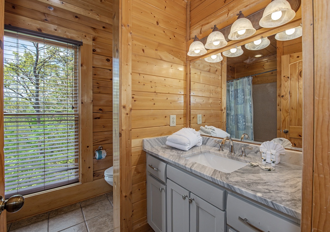 Step into your rustic-modern bathroom with warm wood walls, marble countertops, and fresh towels awaiting your arrival.