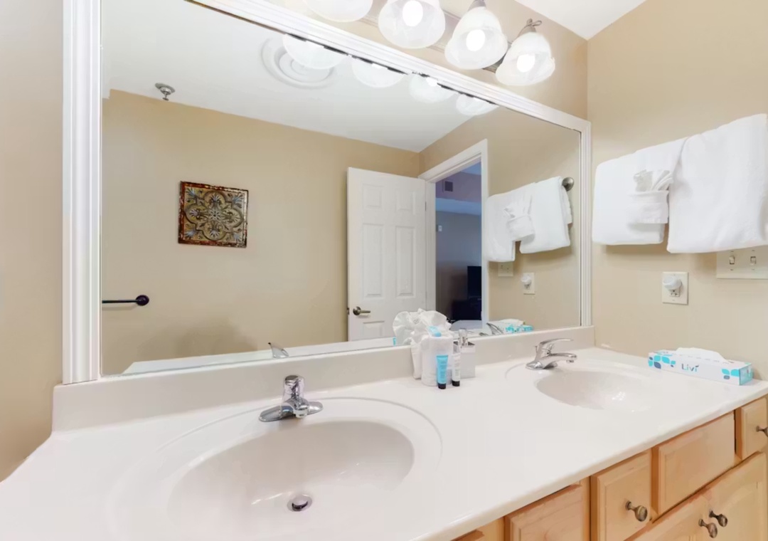 Step into your private bathroom featuring dual sinks, bright vanity lighting, and plush white towels awaiting your morning routine.
