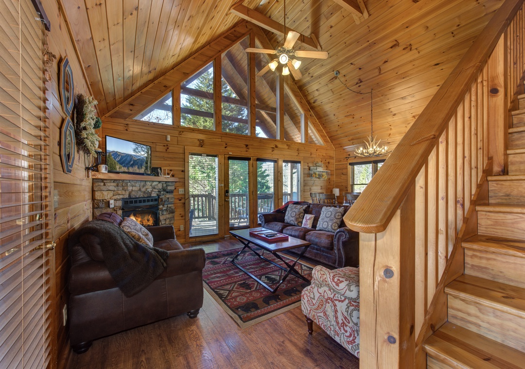 Unwind in your cozy log cabin living room with crackling fireplace, soaring wooden ceilings, and mountain views through floor-to-ceiling windows.