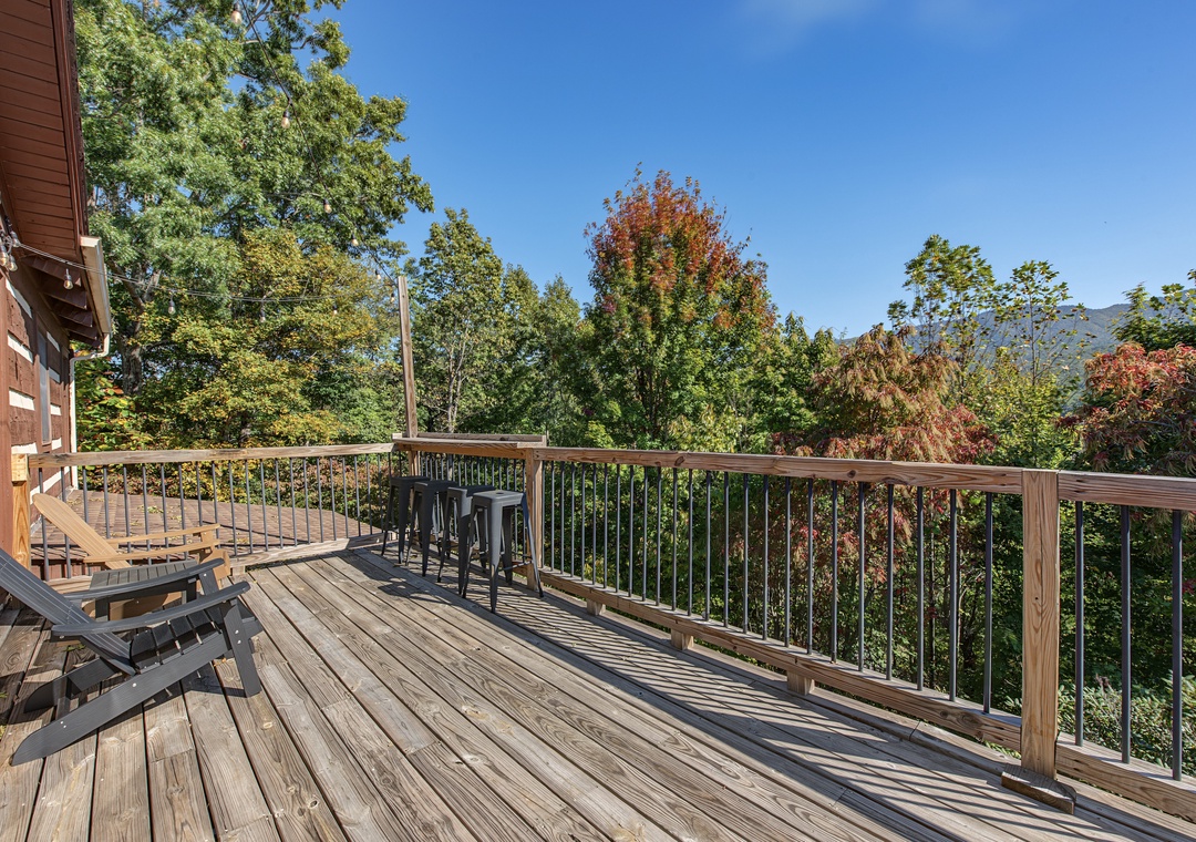 A spacious wooden deck overlooks lush treetops and mountain scenery, offering peaceful outdoor relaxation with ample seating and seasonal color from surrounding foliage.