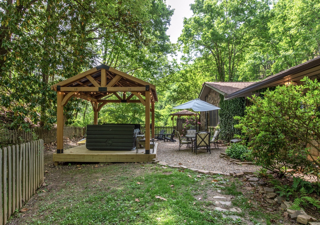 A private backyard retreat features a covered hot tub pavilion, outdoor dining patio, and lush garden surrounded by mature trees—perfect for relaxing evenings under the canopy.