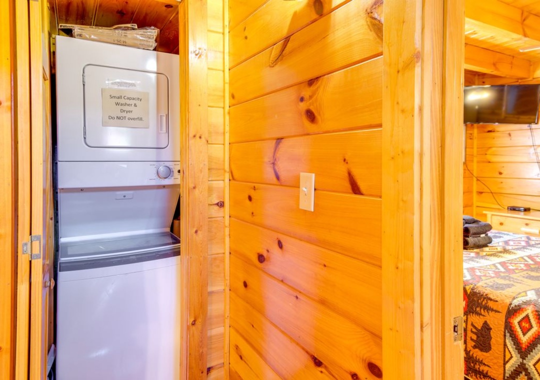 Your cozy cabin features convenient in-room laundry facilities with a compact washer and dryer, nestled within beautiful natural wood walls.