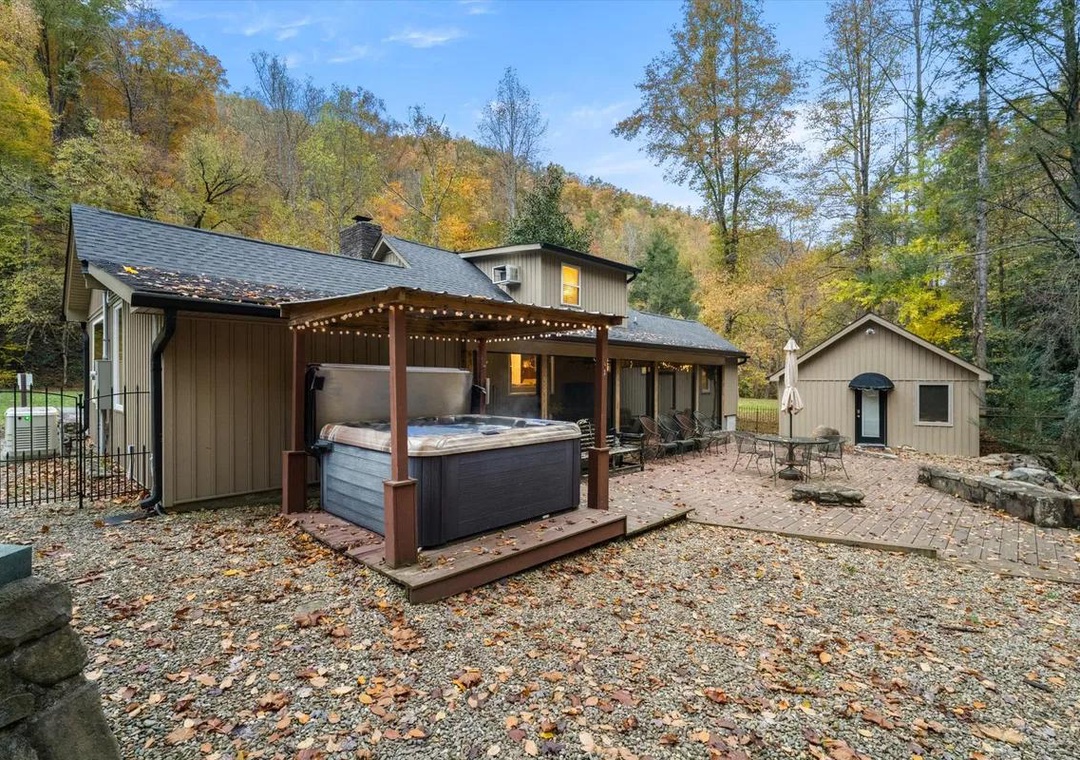 This secluded mountain property features a private hot tub under twinkling lights, surrounded by golden autumn foliage and peaceful forested hills.