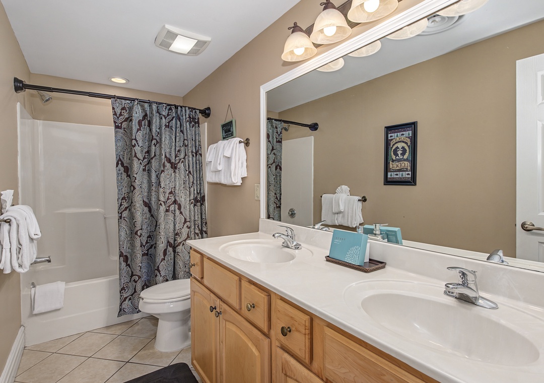 Unwind in your spacious bathroom featuring dual sinks, warm wood vanity, and relaxing tub-shower combo with fresh towels awaiting your arrival.