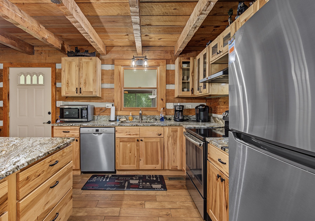 Your fully equipped kitchen features granite countertops, stainless steel appliances, and rustic wood cabinetry beneath exposed beam ceilings—perfect for preparing meals together during your mountain getaway.