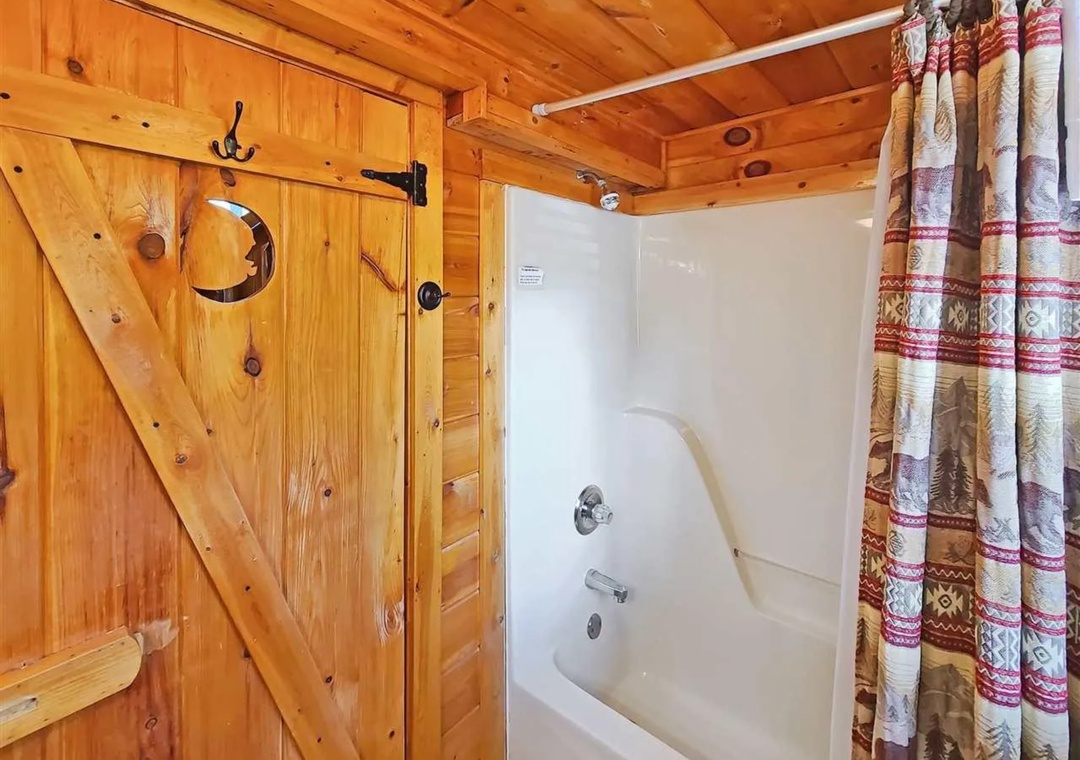 Step into your rustic bathroom where warm knotty pine walls create a cozy cabin atmosphere while you unwind in the spacious tub.