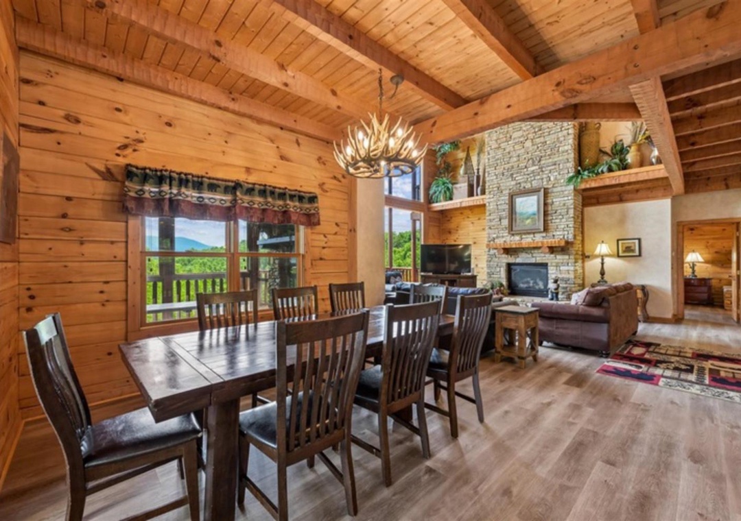 Warm wood beams frame your open-plan living space, where you'll gather around the dining table, relax by the stone fireplace, and enjoy scenic mountain views through expansive windows.