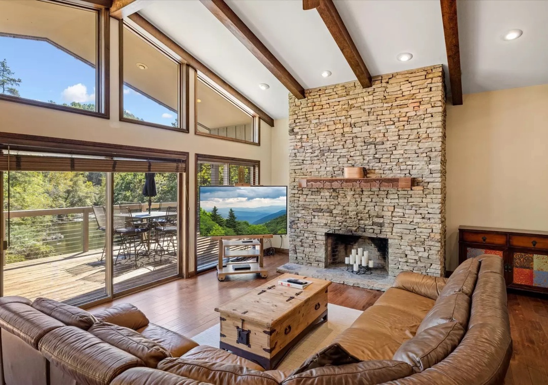 Relax in your stunning living room with vaulted ceilings, stone fireplace, and panoramic mountain views through floor-to-ceiling windows.