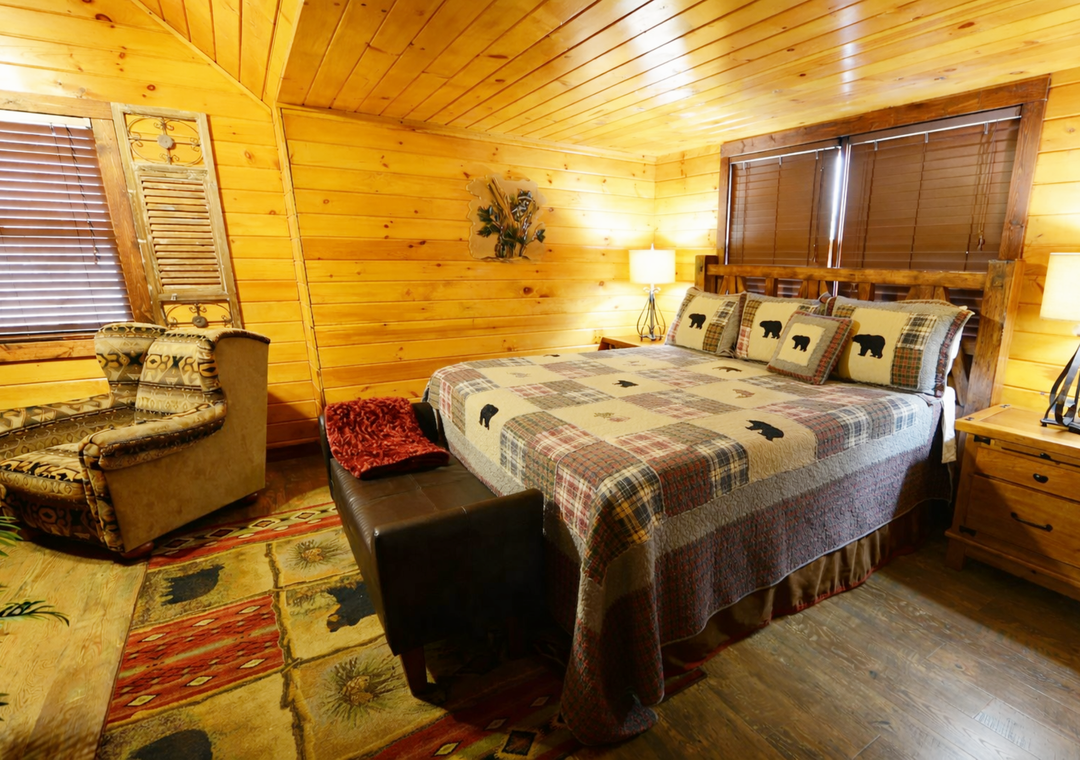 Your cozy cabin bedroom features rustic wood walls, plaid bedding with charming bear motifs, and warm lighting that creates the perfect mountain retreat atmosphere.