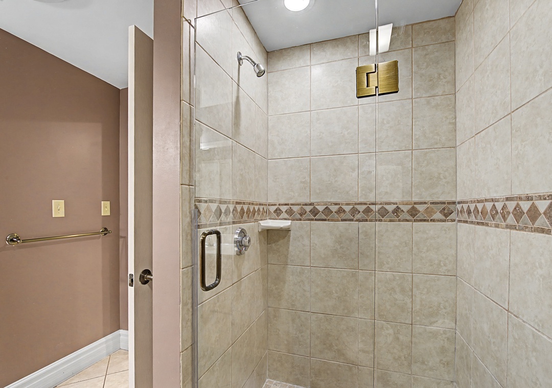 Step into your spacious walk-in shower featuring elegant tiled walls with decorative accents and premium glass doors for your comfort.