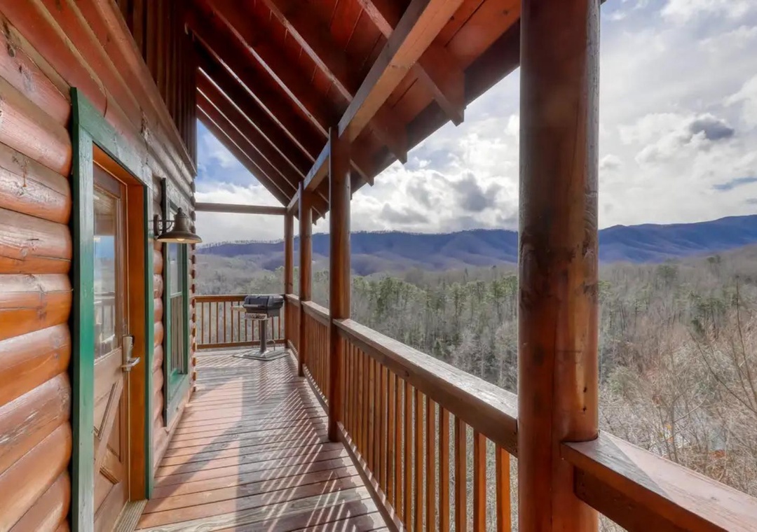 A covered wooden deck showcasing sweeping mountain vistas and forested hillsides, with a grill ready for your outdoor cooking adventures.