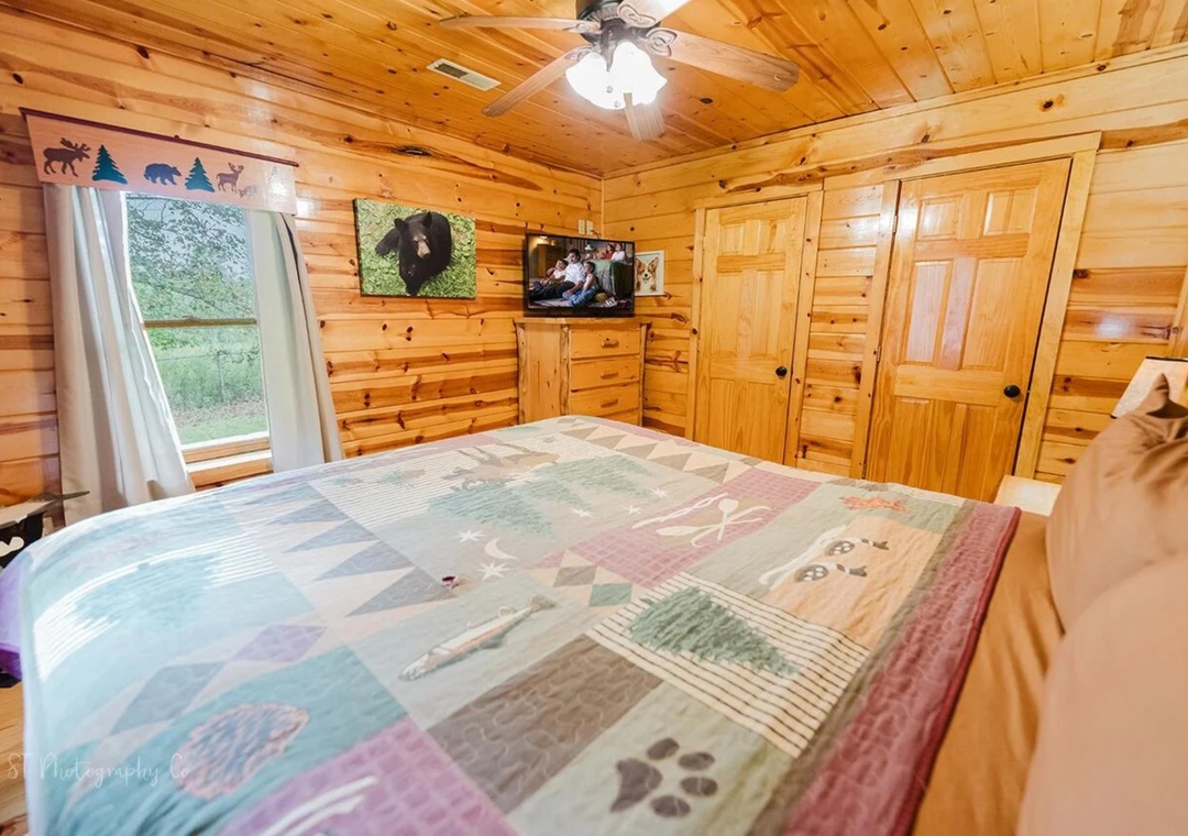 Unwind in your cozy cabin bedroom with rustic wood walls, a comfy bed with nature-inspired linens, and views of the peaceful outdoors through your window.