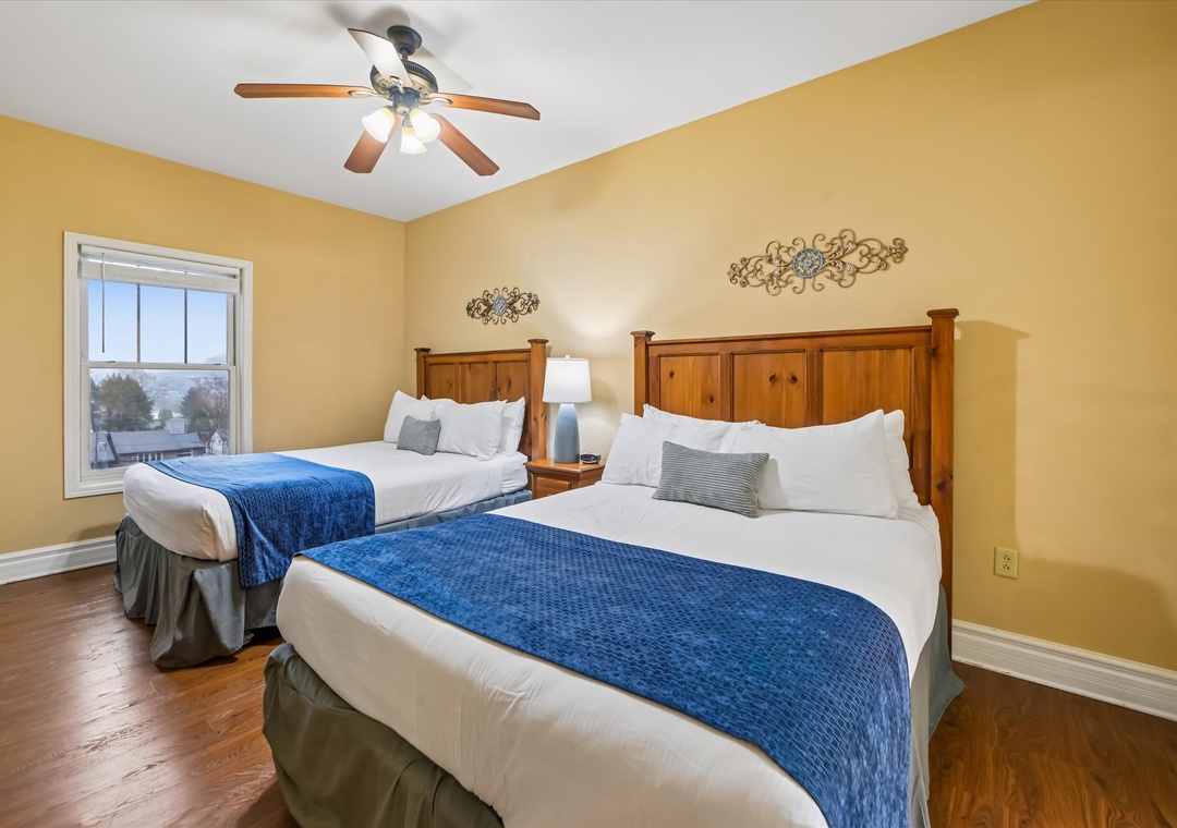 Sink into crisp white linens and cozy blue accents in your sunny twin bedroom, where warm wood tones and gentle ceiling fan create perfect comfort.